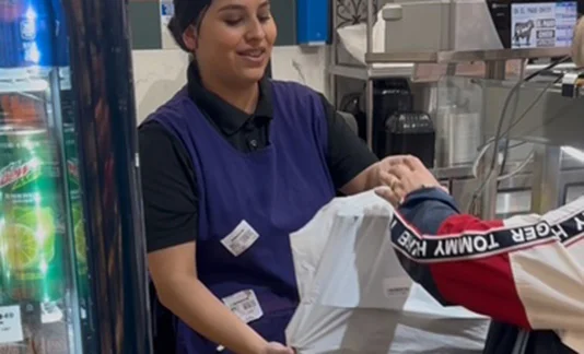 Person in apron handing a bag to someone at a counter